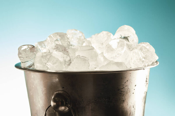 cool ice cubes in metal bucket on emerald and white background