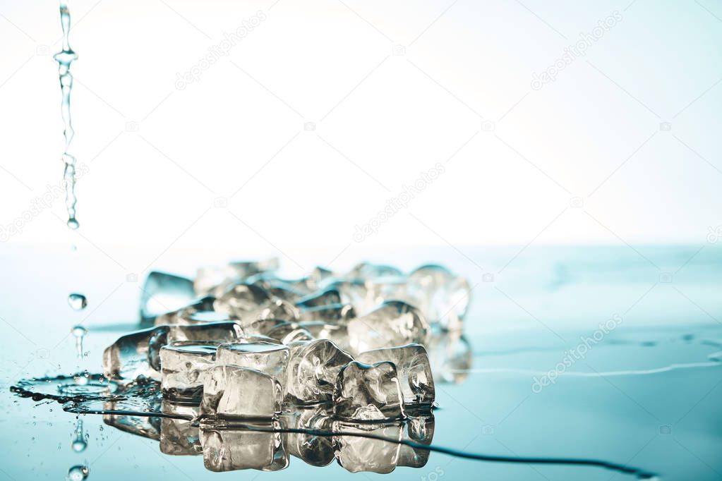 heap of transparent melted ice cubes with water puddles and drops  on emerald and white background