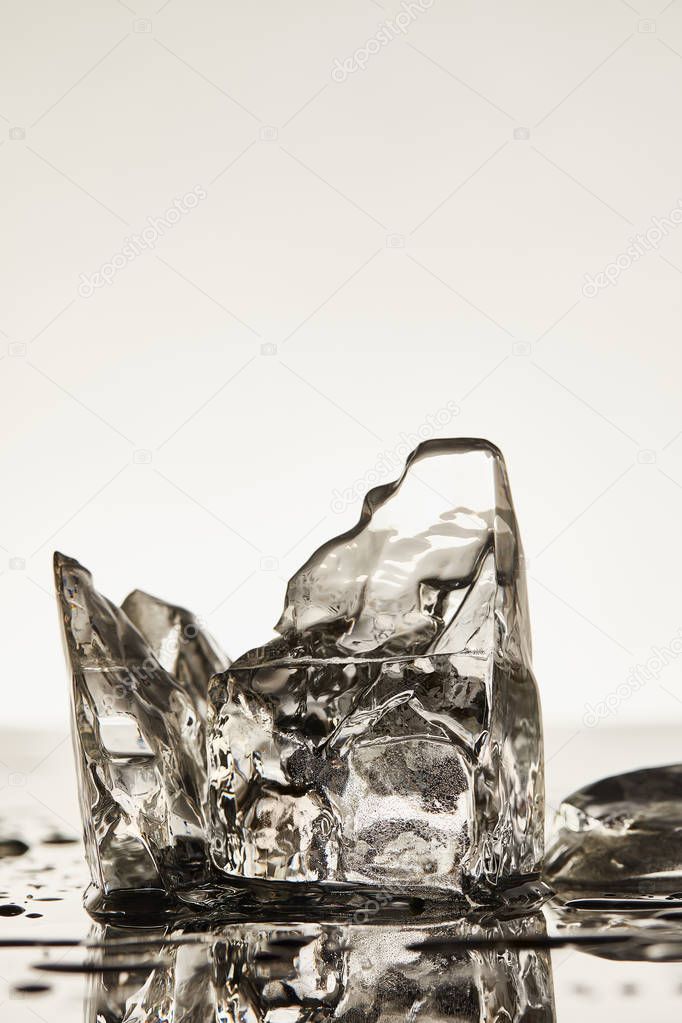 transparent melting ice cubes with drops and puddles on white background