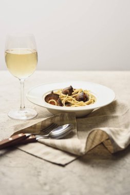 tasty Italian pasta with seafood served with white wine, napkin and cutlery isolated on grey clipart