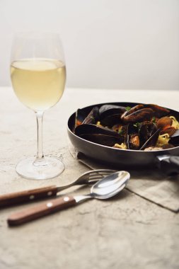 beyaz şarap, peçete ve çatal bıçak takımı gri izole ile tavada sunulan deniz ürünleri ile lezzetli İtalyan makarna