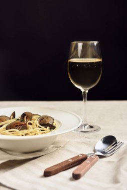 delicious Italian spaghetti with seafood served with white wine on napkin near cutlery isolated on black clipart