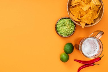 kopya alanı ile turuncu arka plan üzerinde gevrek nachos, guacamole, bira, kireç ve biber üst görünümü