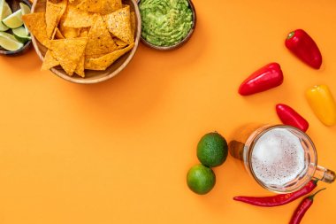 kopya alanı ile turuncu arka plan üzerinde nachos, guacamole, bira, kireç ve biber üst görünümü
