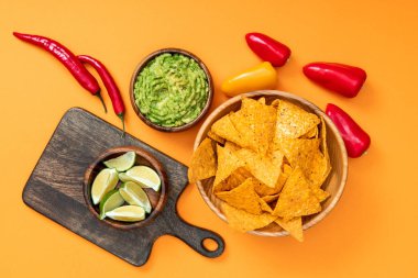 gevrek Meksika nachos üst görünümü, guacamole, biber, limon ve turuncu arka plan üzerinde ahşap kesme tahtası