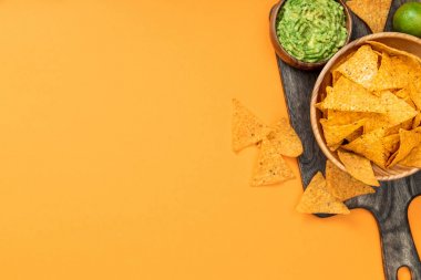 ahşap kesme tahtası üzerinde gevrek Meksika nachos üst görünümü, guacamole ve portakal arka plan üzerinde kireç kopya alanı ile