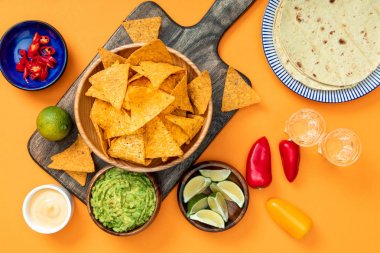 Meksika nachos portakal arka plan üzerinde guacamole, peynir sosu, biber, ıhla, Tekila ve tortilla ile ahşap kesme tahtası üzerinde servis
