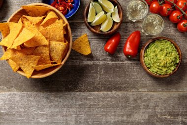 top view of Mexican nachos served with guacamole, vegetables, limes and Tequila on weathered wooden table clipart