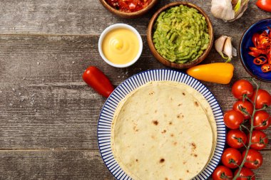 top view of Mexican tortilla with guacamole, cheese sauce and salsa on weathered wooden table with copy space clipart