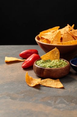 Mexican nachos with guacamole and chili peppers on stone table isolated on black clipart