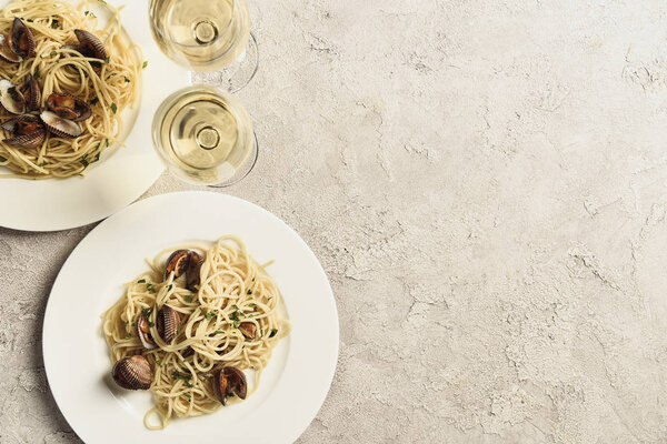top view of delicious pasta with seafood served with white wine in glasses on textured grey surface with copy space