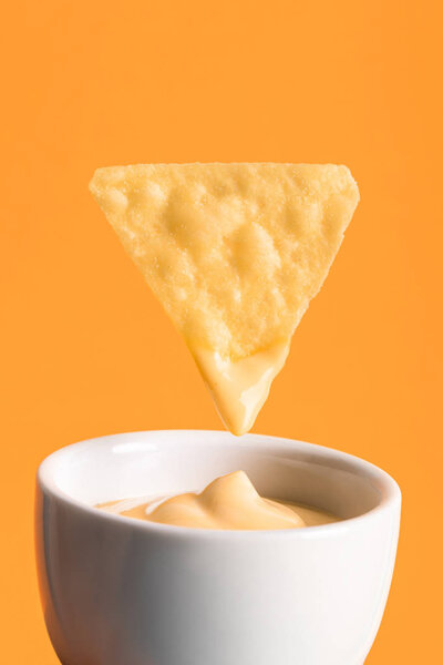 crispy corn nacho with cheese sauce in bowl isolated on orange, Mexican cuisine