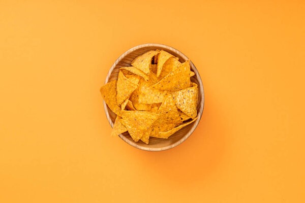 top view of crispy nachos in wooden bowl on orange background, Mexican cuisine