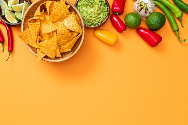 top view of mexican nachos, guacamole and spices on orange background with copy space