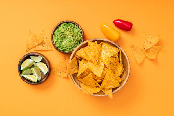 top view of crispy Mexican nachos, guacamole, limes and bell peppers on orange background