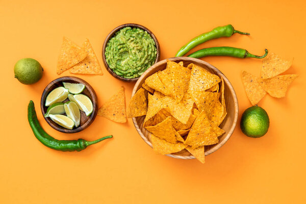 top view of crispy Mexican nachos, guacamole, jalapenos, limes on orange background