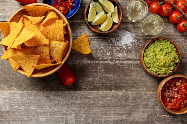 top view of Mexican nachos served with guacamole and salsa on weathered wooden table
