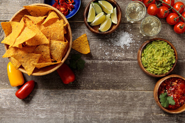 top view of Mexican nachos served with Tequila, guacamole and salsa on weathered wooden table