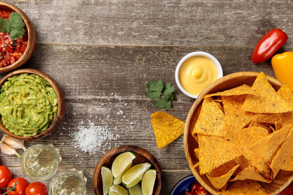 top view of Mexican nachos served with cheese sauce, guacamole and salsa on weathered wooden table