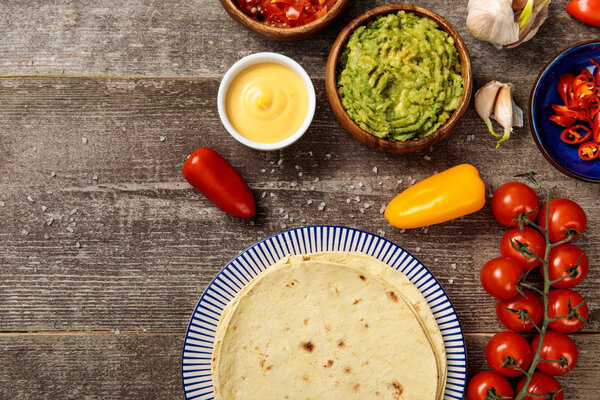 top view of Mexican tortilla with spices, guacamole, cheese sauce and salsa on weathered wooden table
