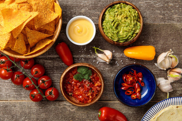 top view of Mexican nachos served with guacamole, cheese sauce and salsa on wooden rustic table
