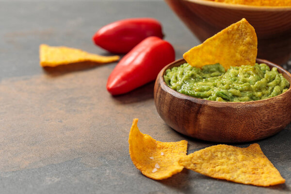 close up view of Mexican nachos with guacamole and chili peppers on stone table with copy space
