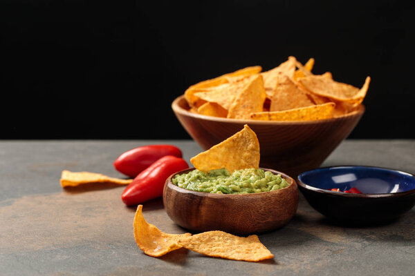 traditional Mexican nachos with guacamole and chili peppers on stone table isolated on black