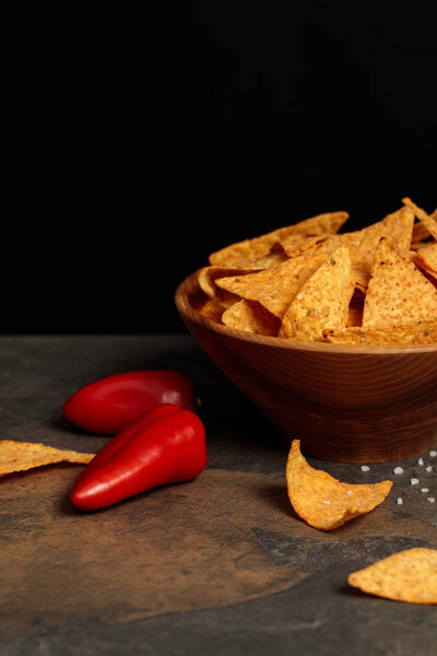 crunchy Mexican nachos with salt and chili peppers on stone table isolated on black