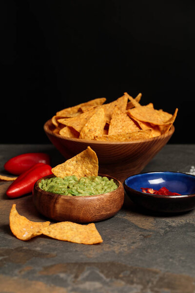 tasty Mexican nachos with guacamole and chili peppers on stone table isolated on black