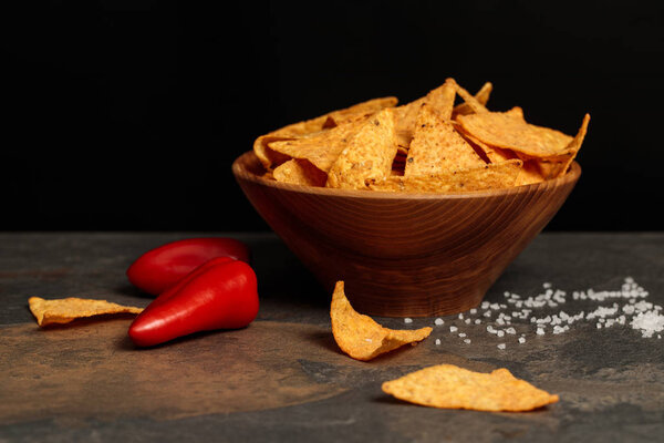 salty Mexican nachos with red chili peppers on stone table isolated on black