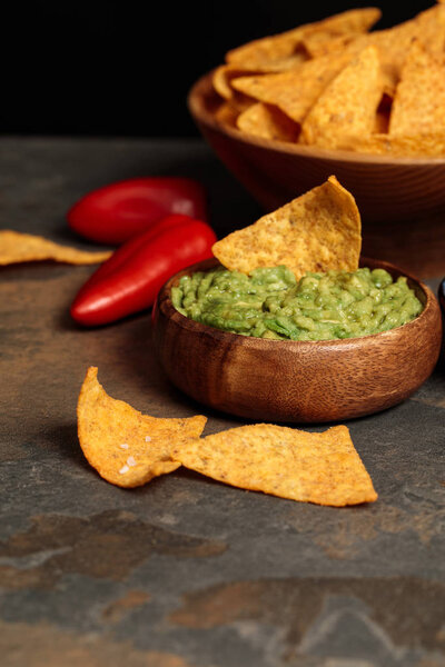 close up view of Mexican nachos with fresh guacamole and chili peppers on stone table isolated on black