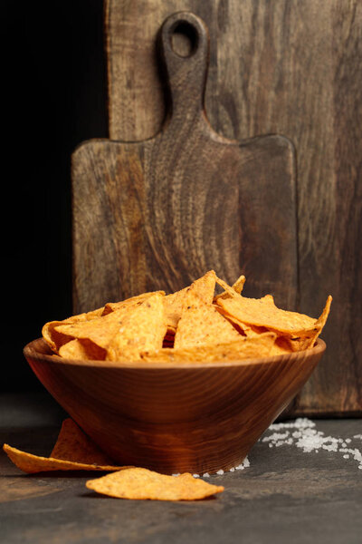 Mexican nachos with salt near wooden cutting boards on stone table isolated on black