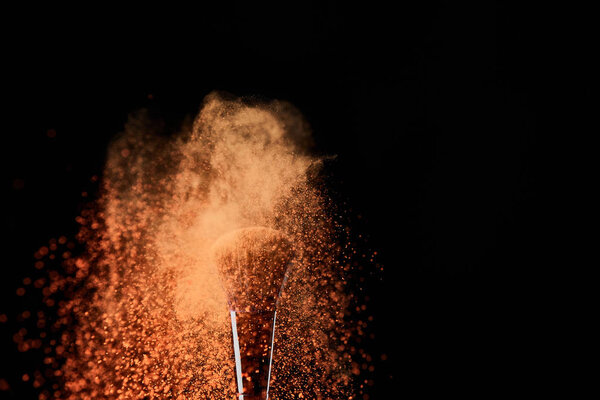 косметическая кисть с оранжевым взрывом порошка на черном фоне
