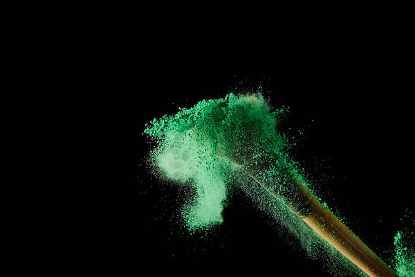 cosmetic brush with colorful green powder explosion on black background