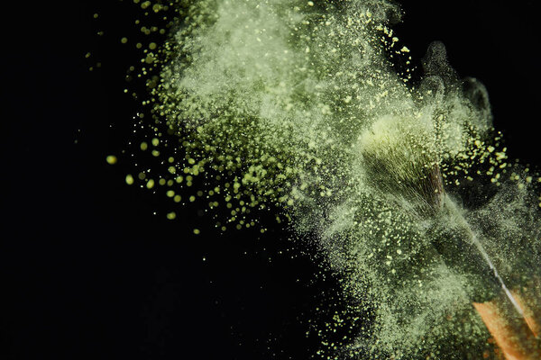 cosmetic brush with yellow powder explosion on black background