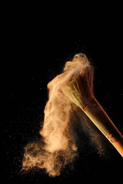 косметическая кисть с разбросанным оранжевым порошком на черном фоне
