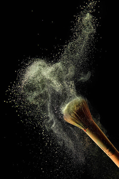 cosmetic brush with yellow colorful powder paint on black background