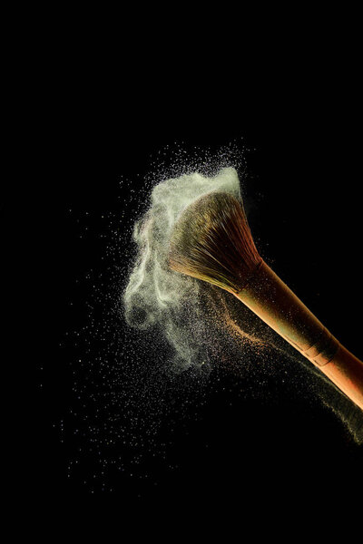 косметическая кисть с желтой красочной пылью на черном фоне
