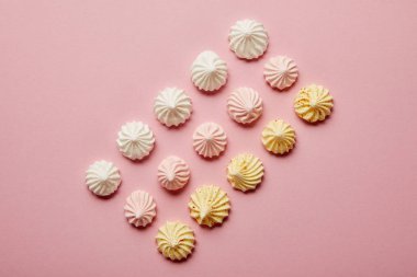 Pembe arka plan üzerinde sıralı beyaz, pembe ve sarı bezelerin üst görünümü
