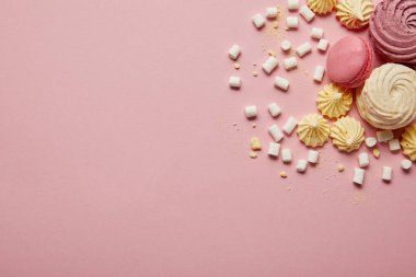 Pembe arka planda pembe tatlı makaronlar, sarı bezeler ve marshmallow'ların üst görünümü