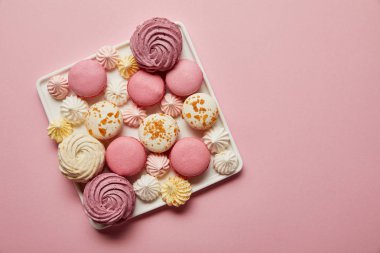 Top view of assorted french macaroons and meringues on square dish on pink background clipart
