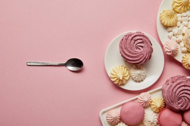 Pembe arka plan üzerinde kaşık ile tatlı bezeler ve macaroons ile Tabaklar 