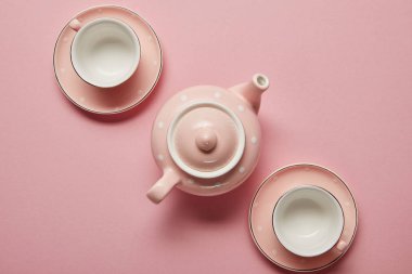 Pastel pink dotted teapot and cups with saucers on pink background clipart