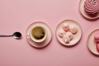 Pembe arka plan üzerinde kaşık ve kahve fincan ı ile pembe noktalı tabaklar üzerinde pembe bezeler ve macaroons üst görünümü