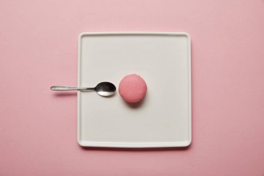Pembe arka plan üzerinde beyaz kare çanak çay kaşığı ile pembe macaroon üst görünümü