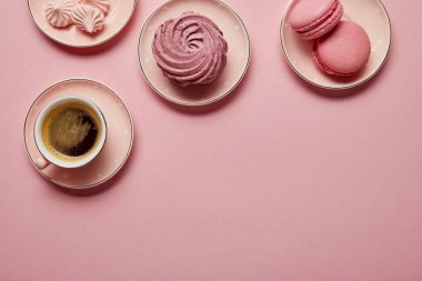 Pembe arka plan üzerinde beyaz nokta lı pembe tabaklar üzerinde pembe bezeler, makaronlar ve bir fincan kahvenin üst görünümü