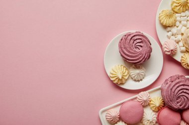 Pembe arka planda pembe, beyaz ve sarı bezeler, makaronlar ve marshmallow'ların üst görünümü