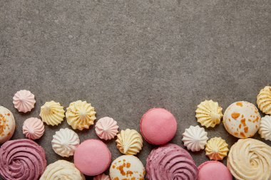 Gri arka planda pembe, sarı ve beyaz bezeler ile pembe ve beyaz makaron üst görünümü