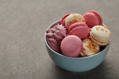 Gri arka plan üzerinde çeşitli macaroons ve pembe zephyr ile Mavi kase