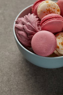 Gri arka plan üzerinde lezzetli pembe ve beyaz makaron ve pembe zephyr ile Mavi kase